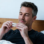 Man sitting up in bed looking at his Snorbliss anti-snoring mouthpiece before sleep