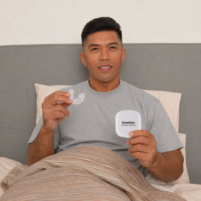 Man sitting up in bed holding the Snorbliss anti-snoring mouthpiece in one hand and its case in the other